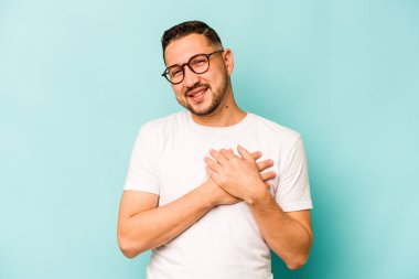 Mavi arka planda izole edilmiş genç İspanyol adam, avuçlarını göğsüne bastıran dostça bir ifadeye sahiptir. Aşk konsepti.