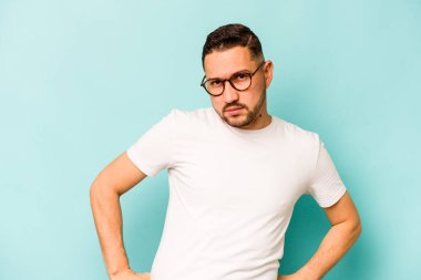 Mavi arka planda izole edilmiş genç bir İspanyol kafası karışmış, kuşkulu ve güvensiz hissediyor..