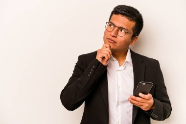 Genç İspanyol iş adamı cep telefonunu beyaz arka planda izole edip şüpheli ve şüpheci bir ifadeyle yana bakıyor..