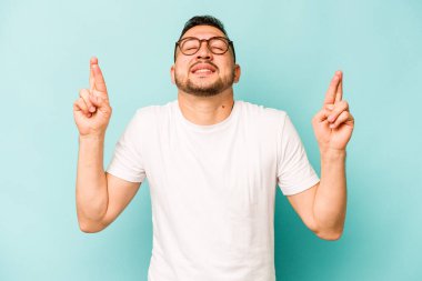 Genç İspanyol adam mavi arka planda izole edilmiş şans dilemek için şans diliyor.