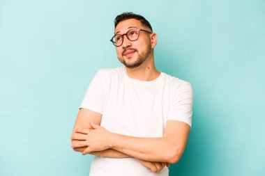 Genç İspanyol adam mavi arka planda izole edilmiş. Amaçlarına ve amaçlarına ulaşmayı hayal ediyor.