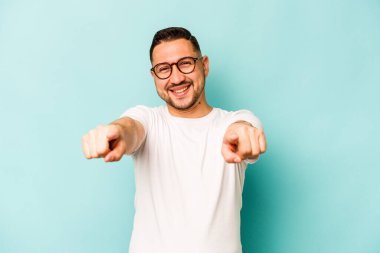 Mavi arka planda izole edilmiş genç İspanyol adam. Önü gösteren neşeli gülücükler..