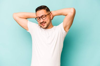 Mavi arka planda izole edilmiş genç İspanyol adam kollarını uzatıyor, rahat bir konumda..