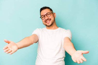 Mavi arka planda izole edilmiş genç bir İspanyol hoş geldin ifadesi sergiliyor..