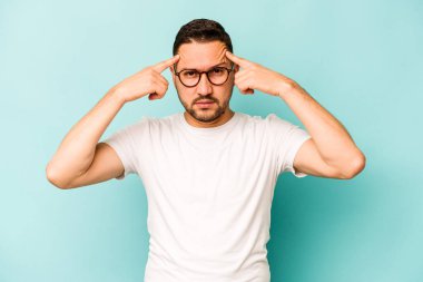 Mavi arka planda izole edilmiş genç İspanyol bir adam bir göreve odaklanmış, işaret parmaklarını işaret ediyor..