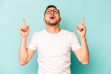 Mavi arka planda izole edilmiş genç bir İspanyol ağzı açık bir şekilde üst tarafı işaret ediyor..