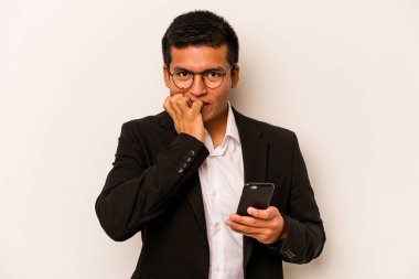 Beyaz arka planda izole edilmiş, tırnak yiyen, gergin ve endişeli bir şekilde cep telefonu tutan genç bir İspanyol iş adamı..