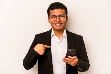 Genç İspanyol iş adamı cep telefonunu beyaz arka planda izole ederek gömlek fotokopi alanını işaret ediyor, gururlu ve kendinden emin.