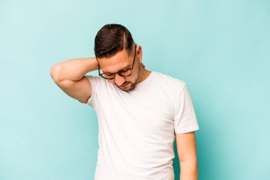 Genç İspanyol bir adam mavi arka planda izole edilmiş, sabit yaşam tarzından dolayı boyun ağrısı çekiyor..