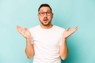 Genç İspanyol adam mavi arka planda izole edildi. Şaşırdı ve şok oldu..