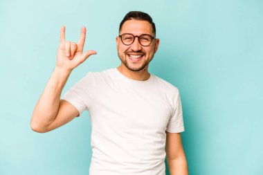 Genç İspanyol asıllı bir adam mavi arka planda izole edilmiş boynuzları bir devrim konsepti olarak gösteriyor..