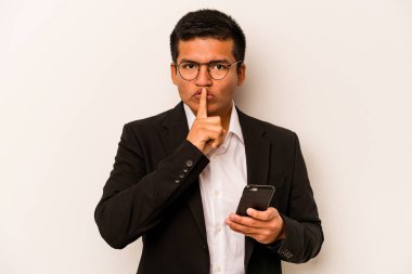 Beyaz arka planda izole edilmiş cep telefonu tutan genç bir İspanyol iş adamı ya sır saklıyor ya da sessizlik istiyor..