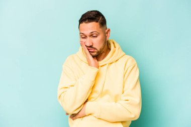 Mavi arka planda izole edilmiş genç bir İspanyol. Sıkılmış, yorgun ve dinlenmeye ihtiyacı var..