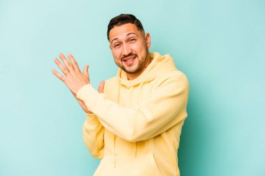 Genç İspanyol adam mavi arka planda izole edilmiş enerjik ve rahat hissediyor, ellerini ovuşturuyor kendinden emin..