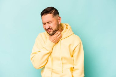 Mavi arka planda izole edilmiş genç İspanyol bir adam virüs ya da enfeksiyon yüzünden boğazında ağrı hissediyor..