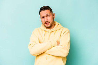 Mavi arka planda kendini güvende hisseden, kararlılıkla kollarını kavuşturan genç İspanyol bir adam..