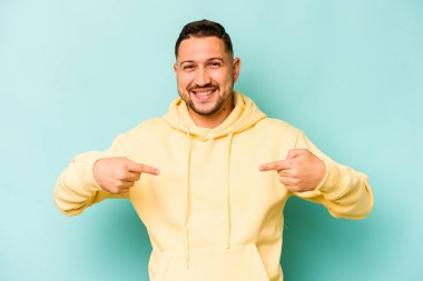 Mavi arka planda izole edilmiş genç İspanyol adam parmağını göstererek şaşırdı, geniş bir gülümsemeyle..