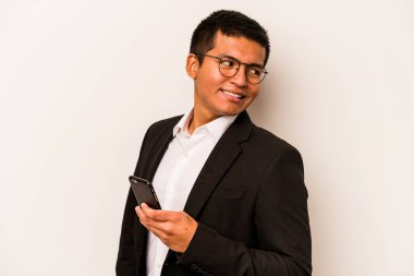 Beyaz arka planda cep telefonu tutan İspanyol genç adam gülümsüyor, neşeli ve keyifli görünüyor..