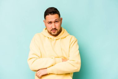 Genç İspanyol bir adam mavi arka planda izole edilmiş şüpheli, belirsiz, seni muayene ediyor..