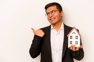 Genç bir İspanyol iş adamı beyaz arka planda küçük bir ev tutuyor. Baş parmak uzakta, gülüyor ve kaygısız..