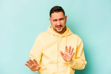 Genç İspanyol bir adam mavi arka planda izole edilmiş, tiksinti gösteren birini reddediyor..