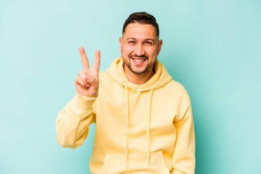 Mavi arka planda izole edilmiş genç İspanyol adam iki numarayı parmaklarıyla gösteriyor..