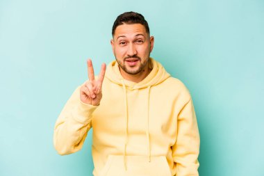 Mavi arka planda izole edilmiş genç İspanyol adam neşeli ve kaygısız parmakları olan bir barış sembolü gösteriyor..