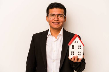 Beyaz arka planda izole edilmiş, mutlu, güler yüzlü ve neşeli küçük bir evi tutan İspanyol bir iş adamı..