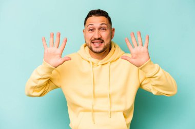 Mavi arka planda izole edilmiş genç İspanyol adam on numarayı elleriyle gösteriyor..