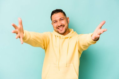 Mavi arka planda izole edilmiş genç İspanyol adam kameraya sarıldığı için kendinden emin hissediyor..