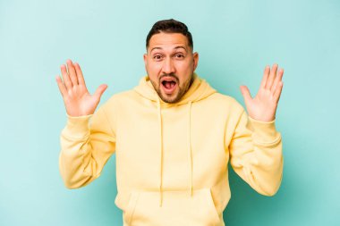 Latin kökenli genç bir adam mavi arka planda zaferi ya da başarıyı kutlarken şaşırmış ve şok olmuştu..