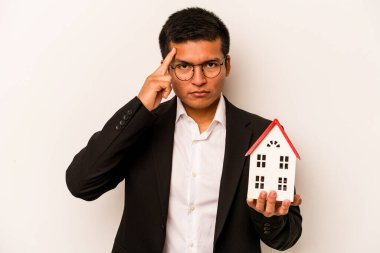 Genç bir İspanyol iş adamı beyaz arka planda küçük bir ev tutuyor. Tapınağı işaret ediyor, düşünüyor, bir göreve odaklanıyor..