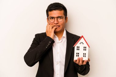 Latin kökenli genç bir adam beyaz arka planda izole edilmiş, tırnak yiyen, gergin ve endişeli bir ev tutuyor..