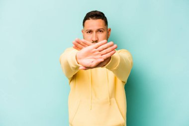 Genç İspanyol bir adam mavi arka planda izole edilmiş, inkar jesti yapıyor.