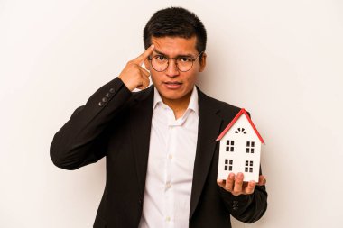 Beyaz arka planda izole edilmiş küçük bir evi tutan İspanyol genç adam işaret parmağıyla yaptığı hayal kırıklığını gösteriyor..