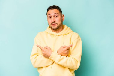 Mavi arka plan noktalarında izole edilmiş genç İspanyol adam iki seçenek arasında seçim yapmaya çalışıyor..