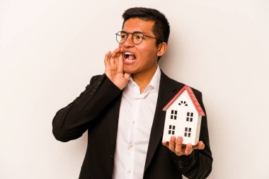 Beyaz arka planda izole edilmiş küçük bir evi tutan İspanyol genç bir adam bağırıyor ve avuç içini açık tutuyor..