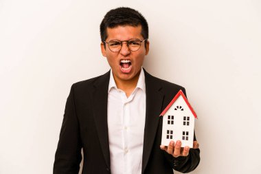 Latin kökenli genç bir adam beyaz arka planda izole edilmiş küçük bir ev tutuyor. Çok sinirli ve agresif bağırıyor..