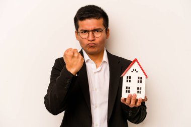 Beyaz arka planda izole edilmiş küçük bir evi tutan İspanyol bir genç kameraya yumruk gösteriyor, agresif bir yüz ifadesi..