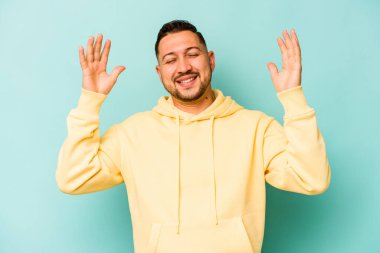 Genç İspanyol adam mavi arka planda izole edilmiş neşeli bir şekilde gülüyor. Mutluluk kavramı.