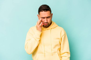 Genç İspanyol adam mavi arka planda izole edilmiş, parmakları dudaklarında bir sır saklıyor..