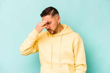Genç İspanyol bir adam mavi arka planda izole edilmiş, başı ağrıyor, yüzüne dokunuyor..