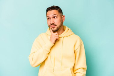 Latin kökenli genç bir adam mavi arka planda izole edilmiş. Bir strateji planlıyor, bir iş yolu düşünüyor..