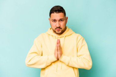Genç İspanyol adam mavi arka planda izole edilmiş dua ediyor, bağlılık gösteriyor, dindar biri ilahi ilhamı arıyor..