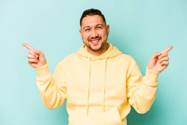 Mavi arka planda izole edilmiş genç İspanyol adam farklı kopya alanlarını gösteriyor, birini seçiyor, parmaklarıyla gösteriyor..