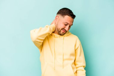 Genç İspanyol bir adam mavi arka planda izole edilmiş. Stres yüzünden boynu ağrıyor. Masaj yapıyor ve elle dokunuyor..