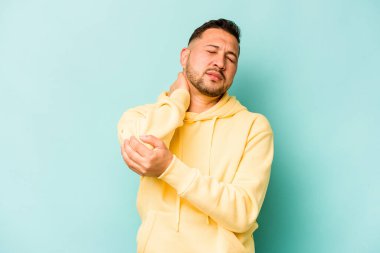 Genç İspanyol adam mavi arka planda izole edilmiş dirsek masajı yapıyor, kötü bir hareketin ardından acı çekiyor..