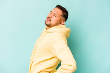 Genç İspanyol bir adam mavi arka planda izole edilmiş sırt ağrısı çekiyor..