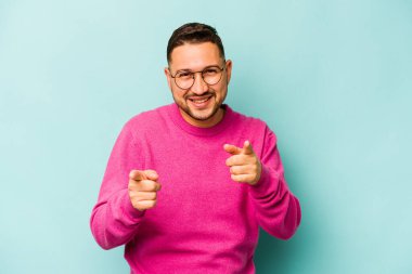 Mavi arka planda izole edilmiş genç İspanyol adam parmaklarıyla öne işaret ediyor..