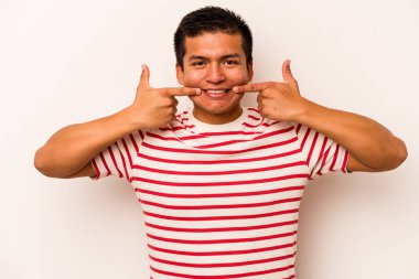 Beyaz arka planda izole edilmiş genç İspanyol adam gülümsüyor, parmaklarını ağıza doğrultuyor..